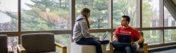 两个学生拿着笔记本电脑坐在窗前聊天